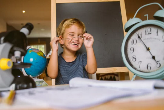 Niño con gafas riendo en escritorio con material escolar